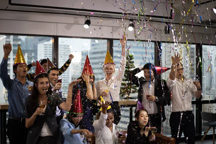 Office employees celebrating with party hats and confetti at a corporate New Year celebration, organized by Joyous Events